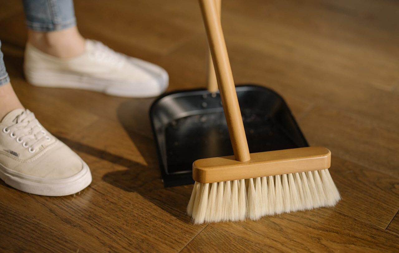 Person Wearing White Pants and White Socks Standing Beside Brown Broom
